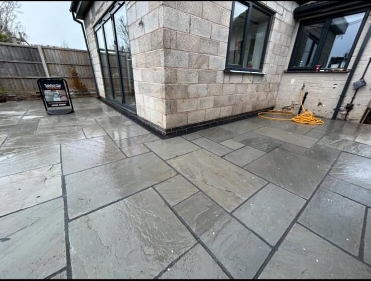 New grey sandstone-effect patio installed around the rear of a house
