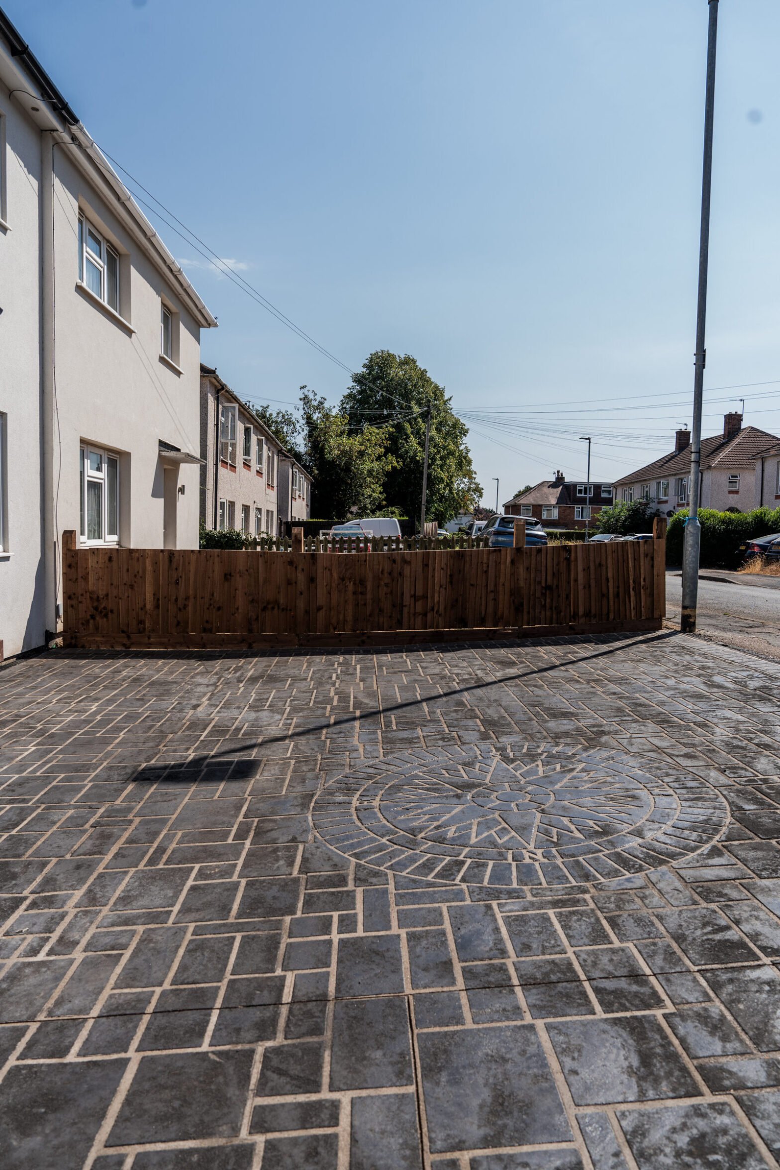 Completed dark pattern-imprinted concrete driveway with circular feature and timber fencing